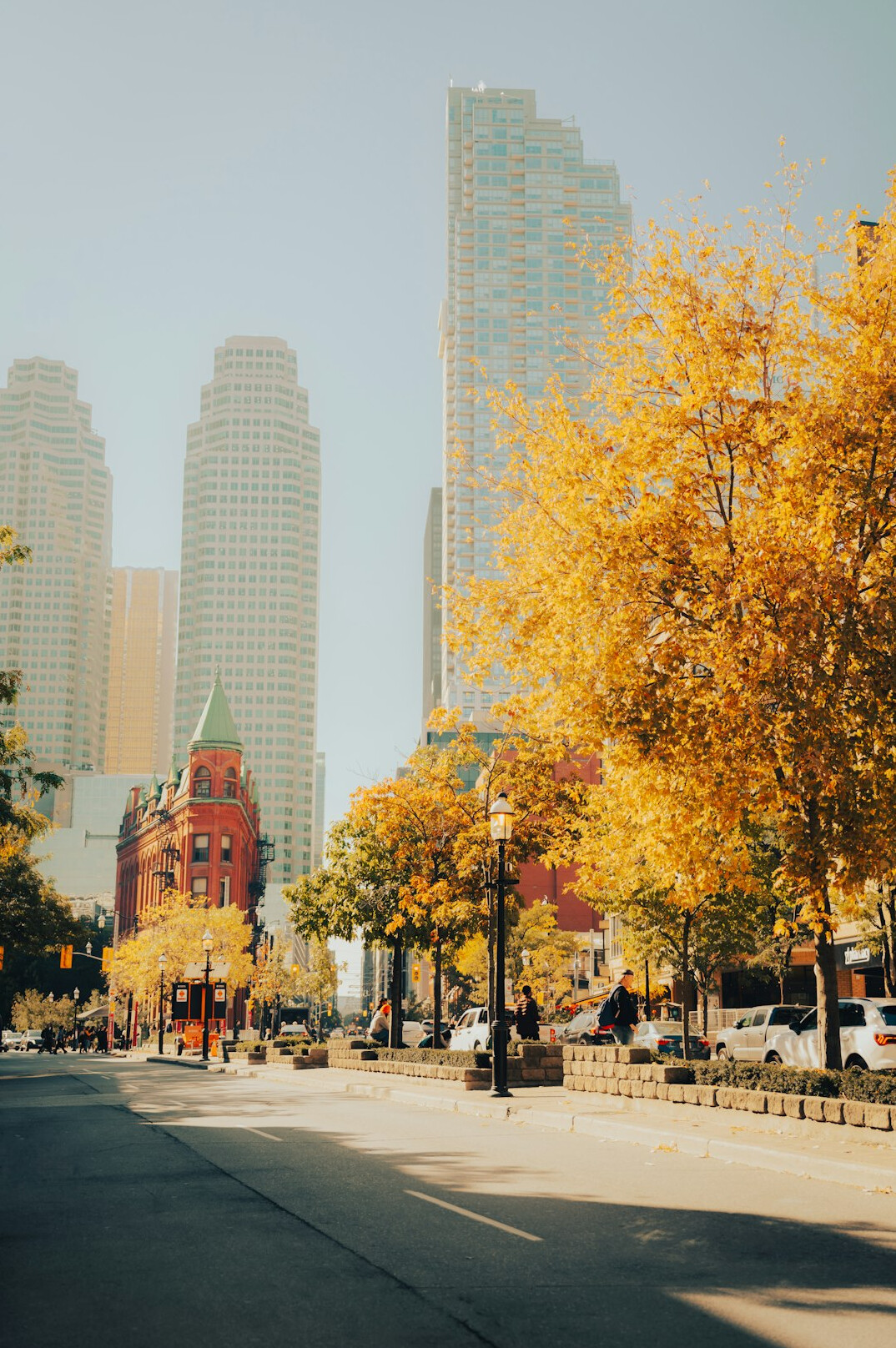 Pedestrians of different backgrounds crossing a busy downtown Toronto street lined with historic brick buildings at golden hour