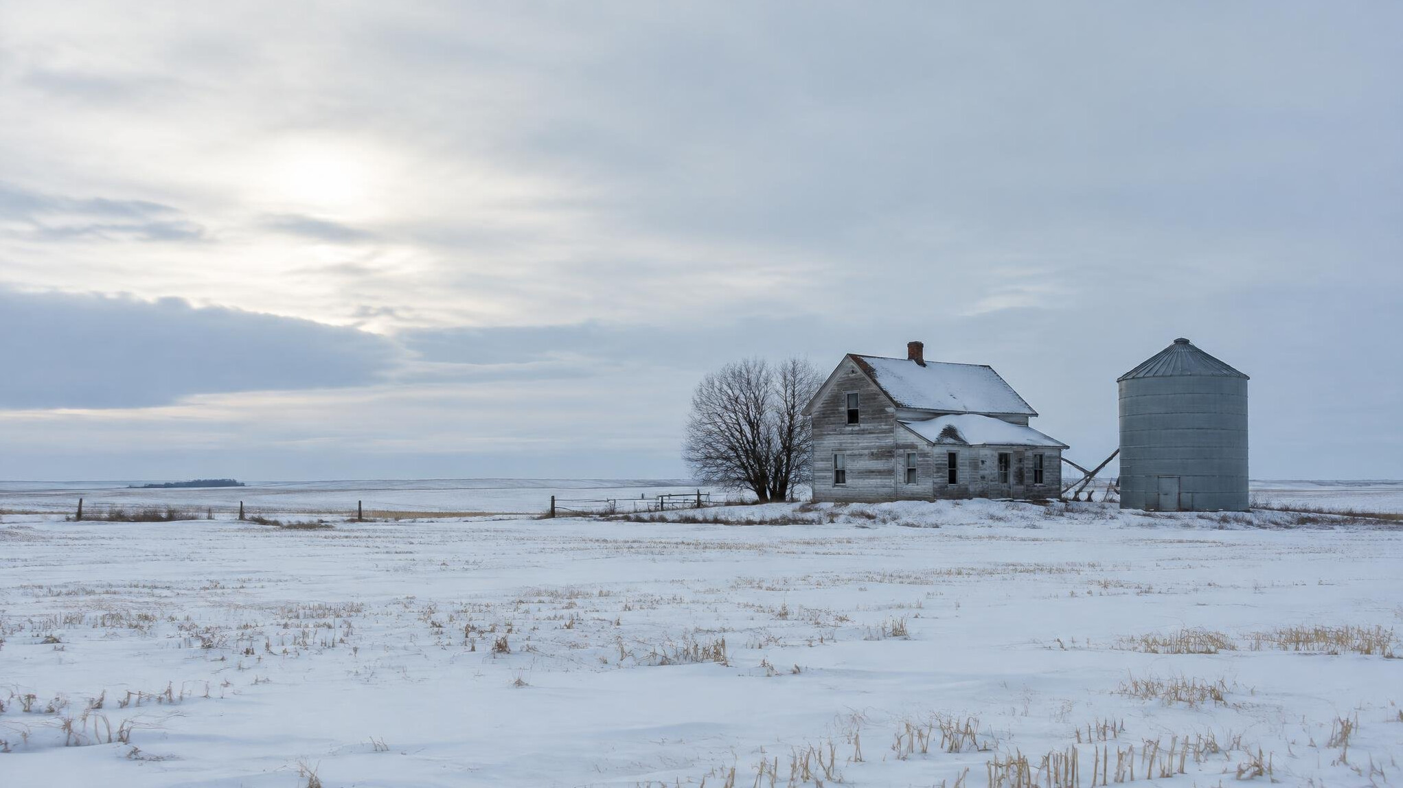A lone farmhouse and grain silo on the snow-covered Saskatchewan prairie under a wide winter sky